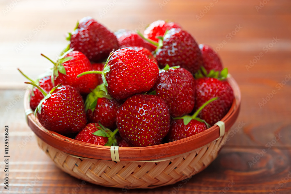 Very beautiful background with fresh strawberries in a wicker round osier basket on old brown wooden background Very beautiful background with fresh strawberries in a wicker round osier basket on old brown wooden background