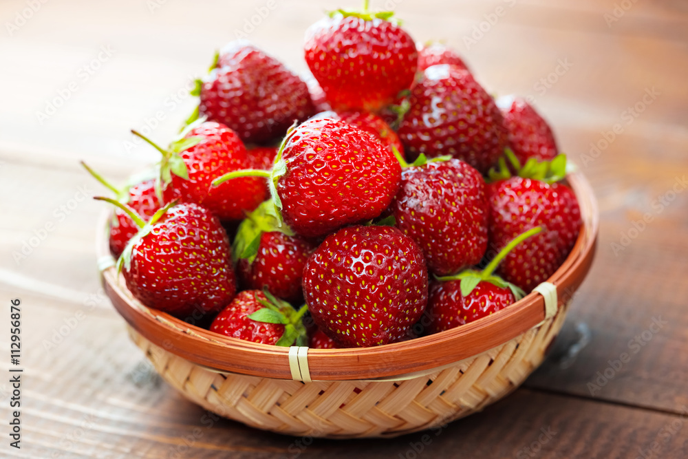 Very beautiful background with fresh strawberries in a wicker round osier basket on old brown wooden background