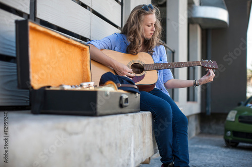 Female street musician sitting on ledge, tuning guitar photo