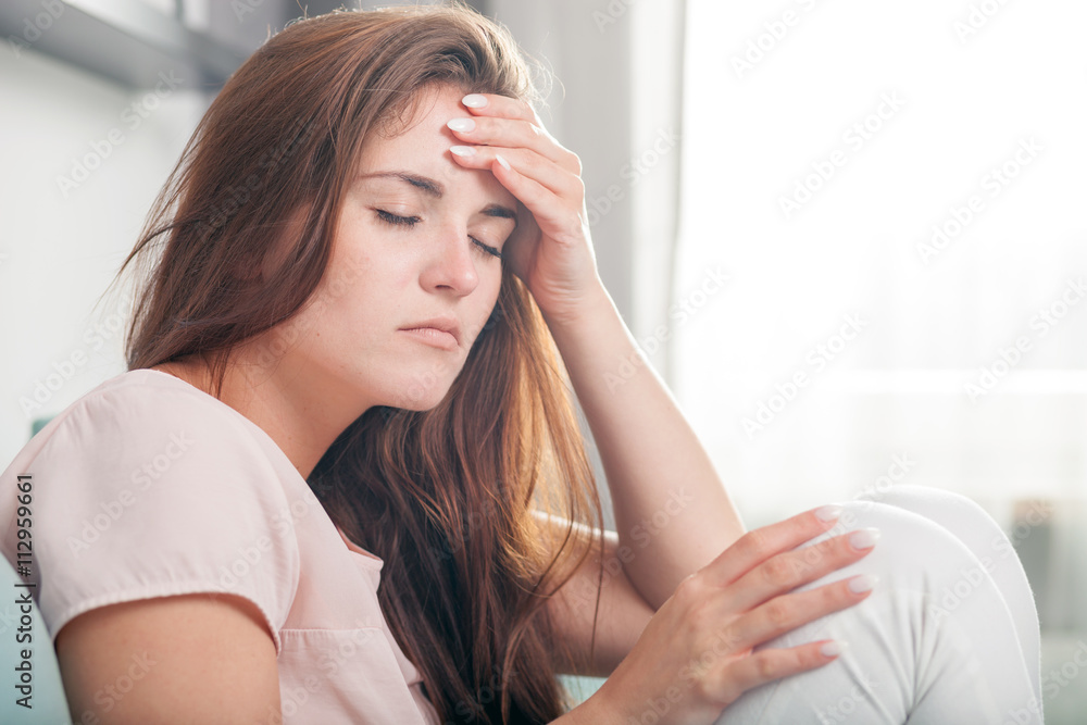 Young woman with headache lying on couch at home. Casual style indoor shoot