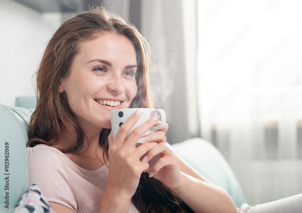 Smiling woman sitting on couch at home and drinking coffee. Casual style indoor shoot Smiling woman sitting on couch at home and drinking coffee. Casual style indoor shoot