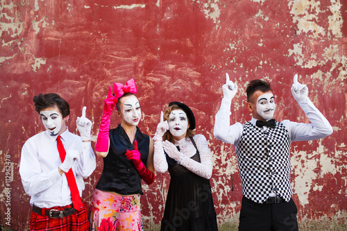 Four mimes point to the top on a red wall.
