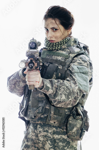 Angry army soldier aiming rifle while standing against white background photo