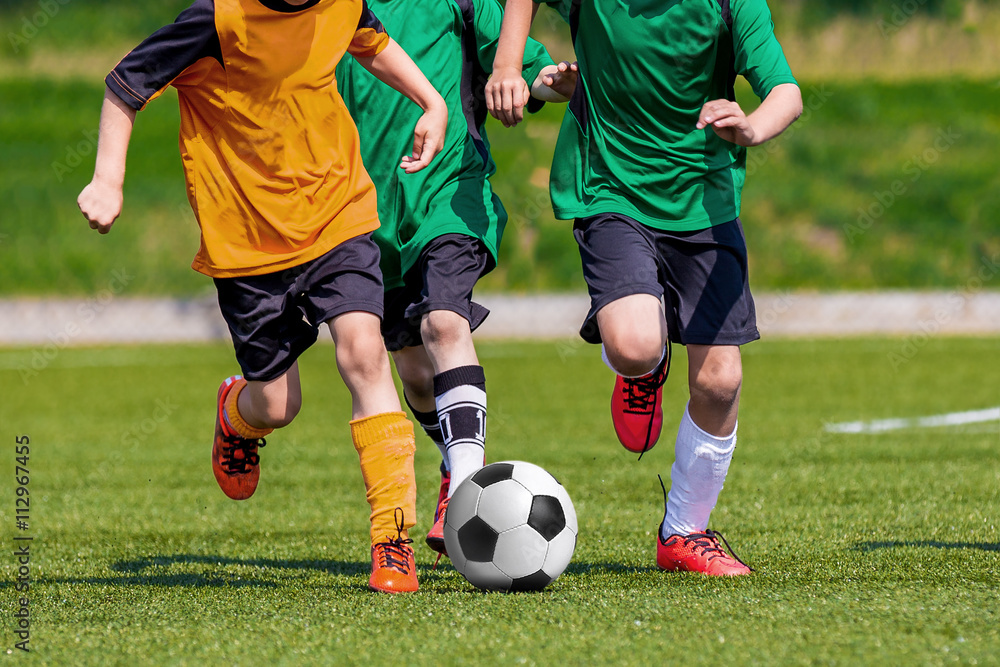 Young boys playing football soccer game on sports field. Running players in colorful green and yellow uniforms. Kids running and kicking soccer ball