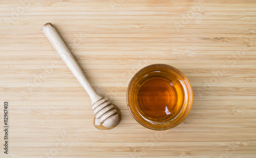 Top view - Glass cup of honey and honey dipper on wooden background