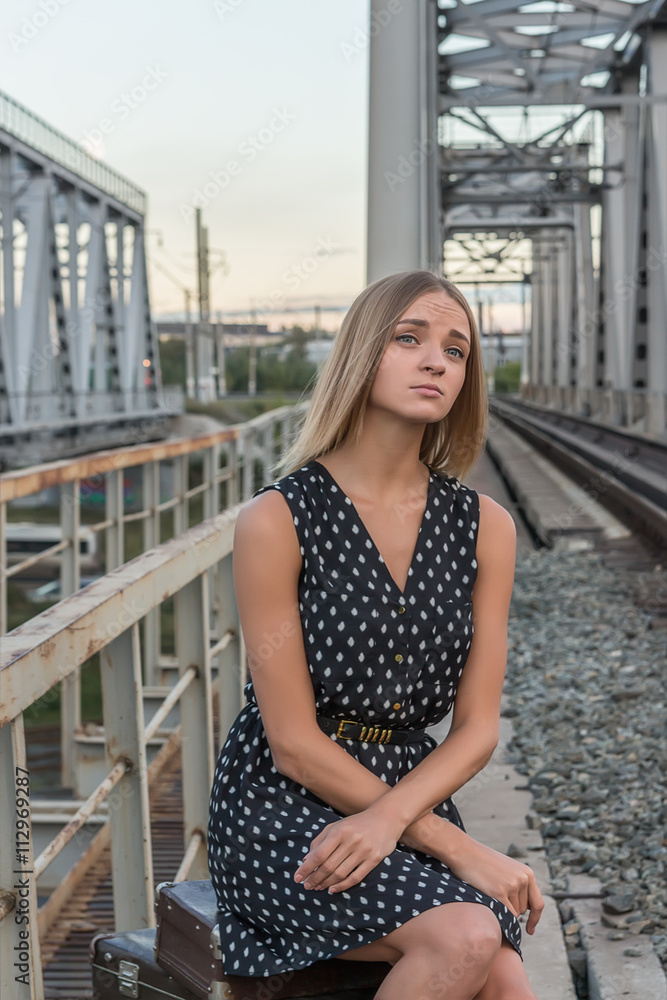 girl sitting waiting for the train looking into the distance the rails of the bridge Peron