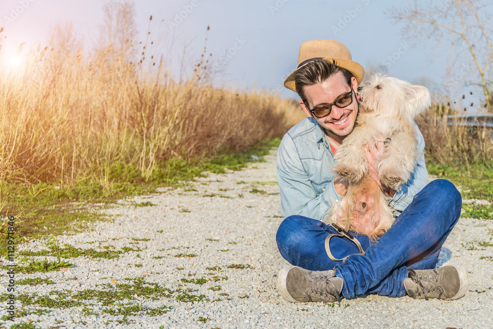 A young and caucasian man with his puppy and white dog, sitting in a park lifestyle, people, nature and animal concept A young and caucasian man with his puppy and white dog, sitting in a park lifestyle, people, nature and animal concept