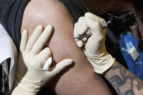 A tattoo artist preparing to tattoo a man's bare arm, close-up photo