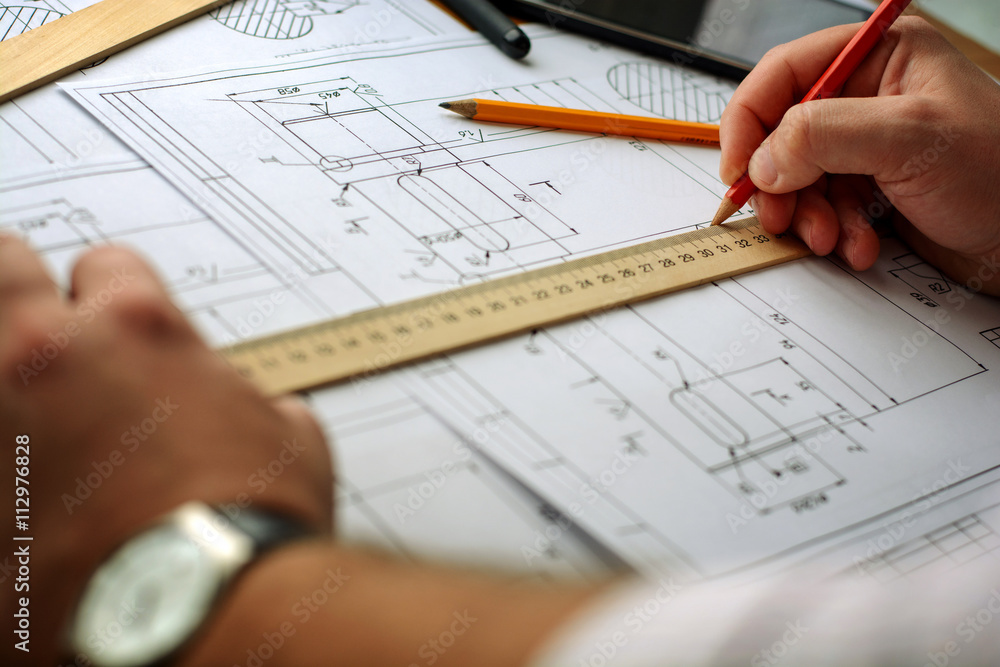 Man architect draws a plan, graph, design, geometric shapes by pencil on large sheet of paper at office desk Man architect draws a plan, graph, design, geometric shapes by pencil on large sheet of paper at office desk