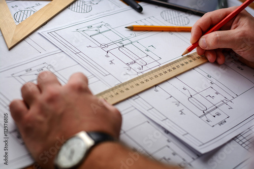 Man architect draws a plan, graph, design, geometric shapes by pencil on large sheet of paper at office desk