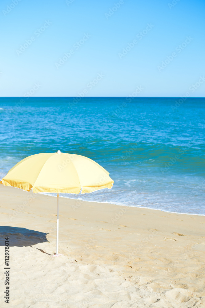 Yellow parasol on desert ocean beach over blue sky