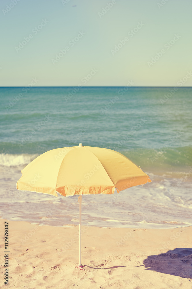 Yellow parasol on desert ocean beach over blue sky