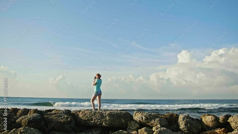 Young woman with red hair in glasses photographs sea standing on the rocks , beach of Dominican Republic, wide angle, slow-motion Young woman with red hair in glasses photographs sea standing on the rocks , beach of Dominican Republic, wide angle, slow-motion
