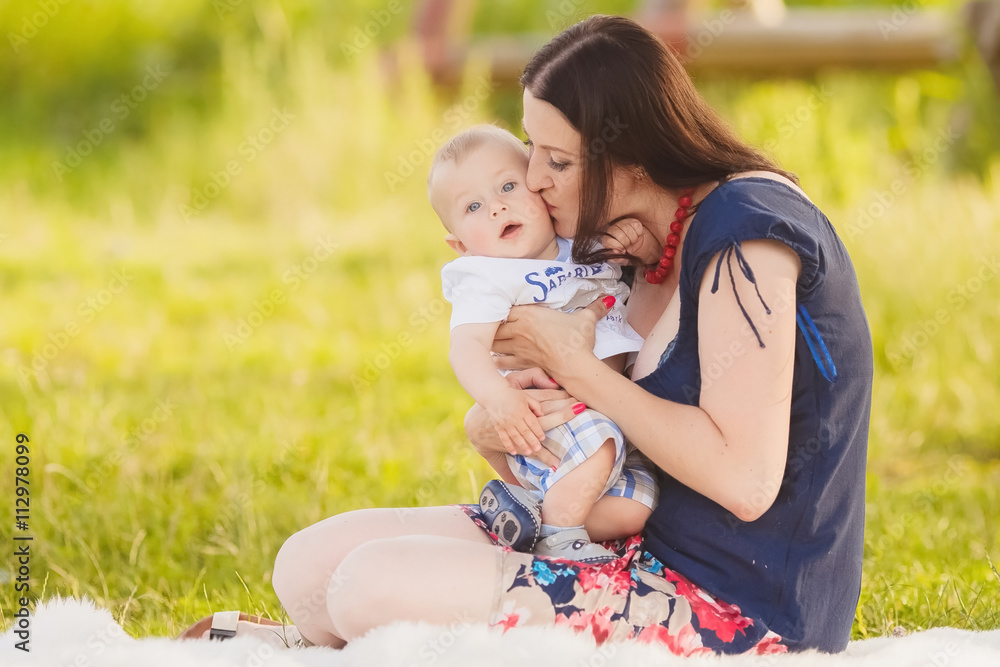 Cute little baby in summer park with mother on the grass. Sweet baby and mom outdoors. Smiling emotional kid with mum on a walk. Smile of a child Cute little baby in summer park with mother on the grass. Sweet baby and mom outdoors. Smiling emotional kid with mum on a walk. Smile of a child