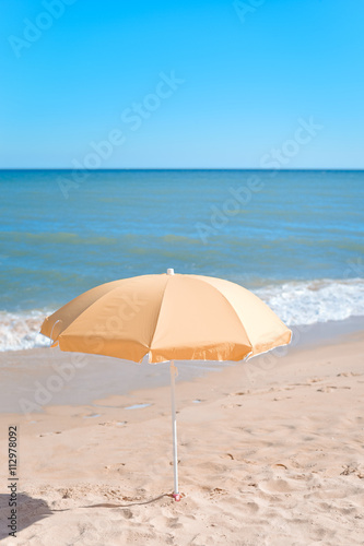 Yellow parasol on desert ocean beach over blue sky