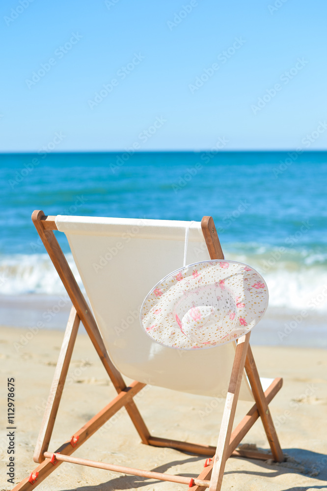 Deckchair and female hat on stunning tropical beach vacation background Deckchair and female hat on stunning tropical beach vacation background