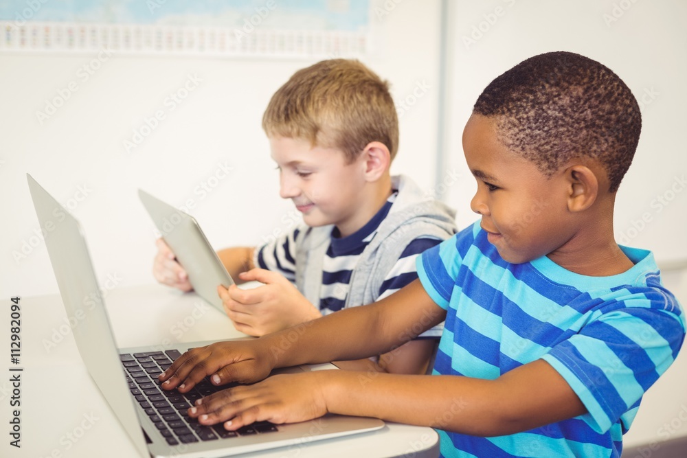 School kids using a laptop and digital tablet in classroom School kids using a laptop and digital tablet in classroom