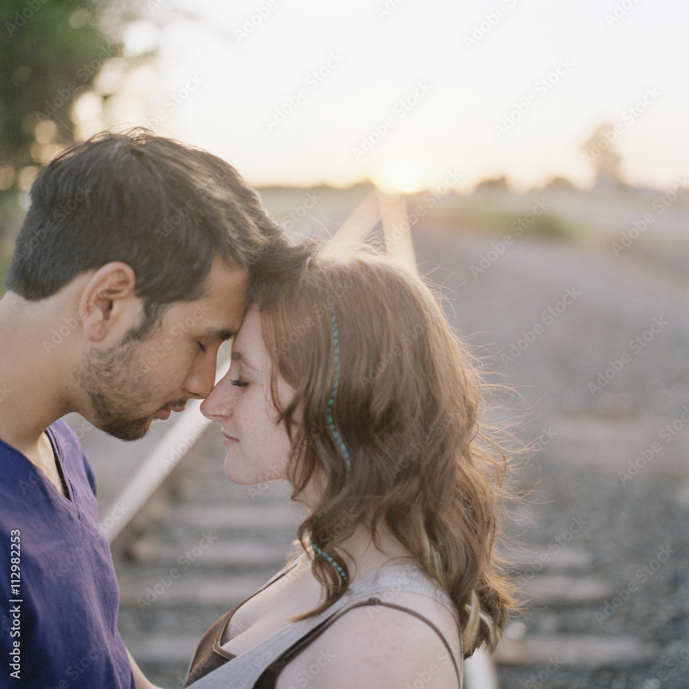 A young couple touching foreheads near railroad track A young couple touching foreheads near railroad track