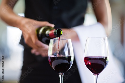 Cuadro en lienzo Mid section of waitress pouring red wine in a glass