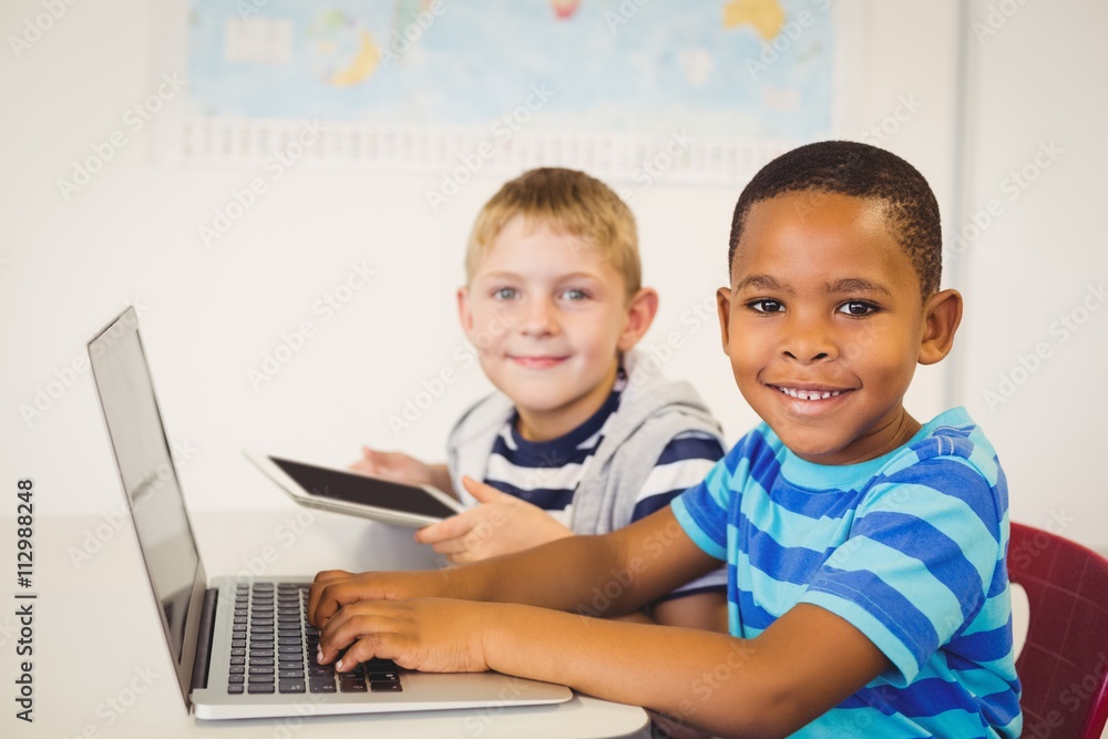Portrait of kids using a laptop and digital tablet in classroom Portrait of kids using a laptop and digital tablet in classroom