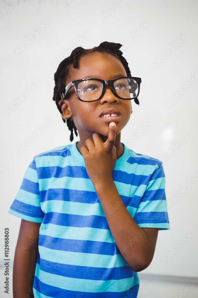 Thoughtful schoolboy standing with hand on chin in classroom Thoughtful schoolboy standing with hand on chin in classroom