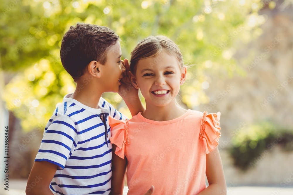 Happy boy whispering a secret in girls ear
