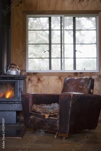 A well worn leather armchair next to a wood burning stove photo