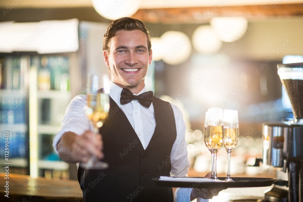 Portrait of smiling waiter offering a glass of champagne 