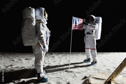 Two astronauts on the moon, an American flag in between them photo