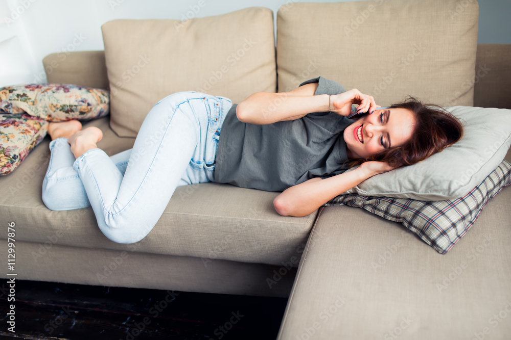 Obraz premium Happy smiling woman talking on cellphone lying on couch.
