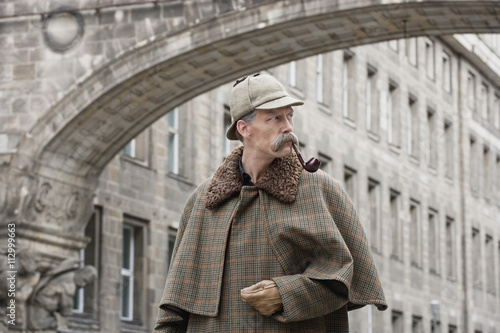 A man dressed up as Sherlock Holmes standing under a building arch looking away photo