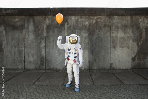 An astronaut on a city sidewalk holding a balloon photo