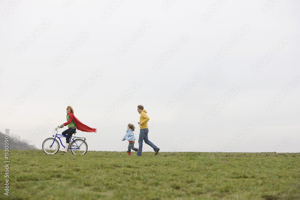 A boy and a man chasing a woman riding a bike A boy and a man chasing a woman riding a bike