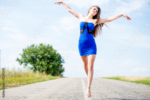exciting flying like bird: portrait of beautiful brunette young woman having fun jumping high on the road on blue sky outdoors copy space background