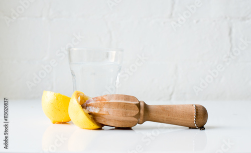 фотографія Lemon halves and citrus reamer in front of glass of water on white table against