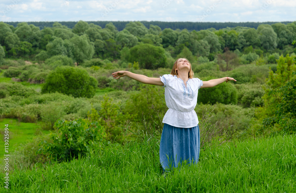 Happy girl stands on background of field with bushes and looks up at sky