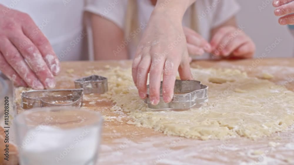 Close of hands of man and two little girls cutting out cookies from dough with metal cutters Close of hands of man and two little girls cutting out cookies from dough with metal cutters