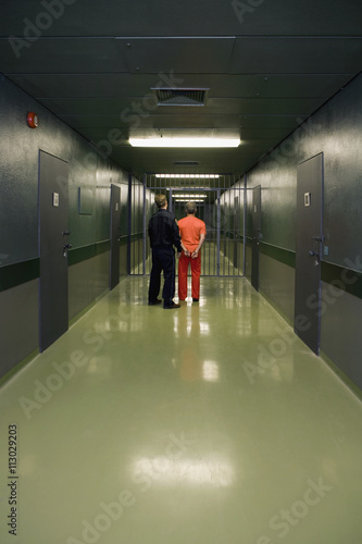 Rear view of prisoner and guard standing in corridor
