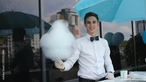 Young guy making cotton candy on a special machine, it wears bow tie, behind him balloons photo