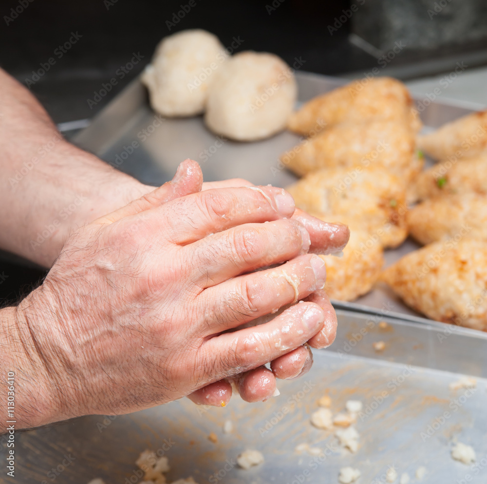 Hand of a cook holding an open typical rice arancino with chicken before modelling it in a cone shape
