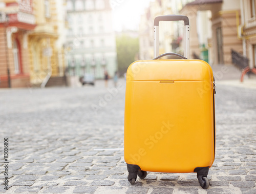 Orange suitcase on the road in city. Summer vacation and travel concept