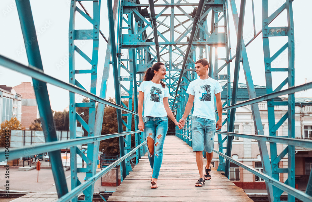 Young couple posing and talking on the old blue metal bridge. Couple dressed in white shirts with their photos. Couple in blue jeans.