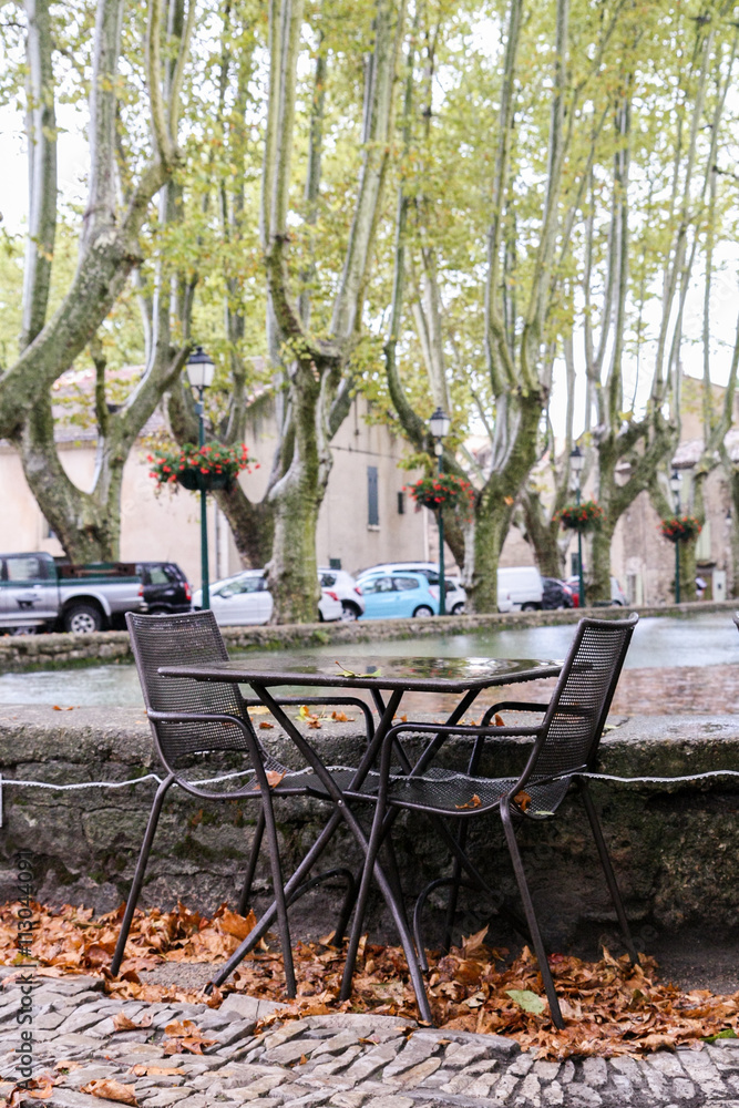 Tables and chairs of street cafes in the town square Luberon among the plane trees in the rain fall.