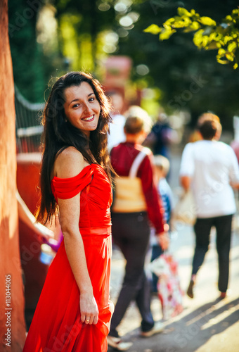 Beautiful brunette girl in red dress with long healthy hair posing on the street