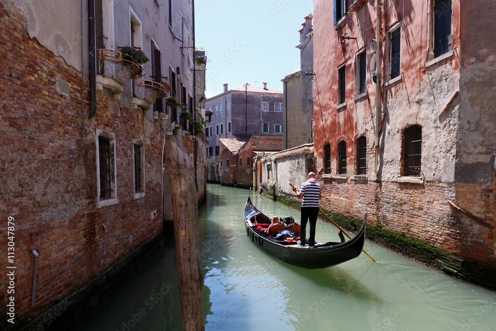 Venetian gondolier punting gondola through canal waters of Venic