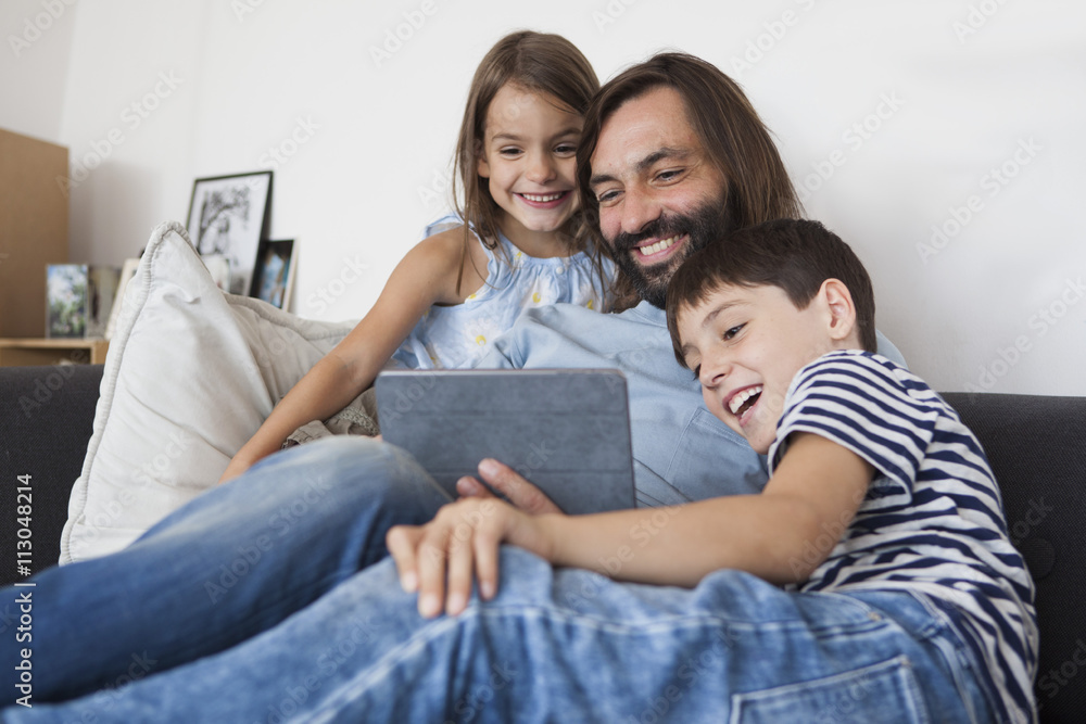 Happy father with children using digital tablet on sofa at home Happy father with children using digital tablet on sofa at home