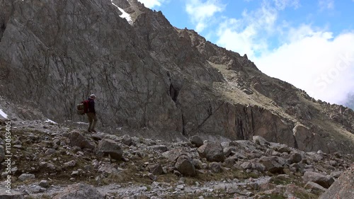 Hiker with red backpack walking along rock 4K video photo