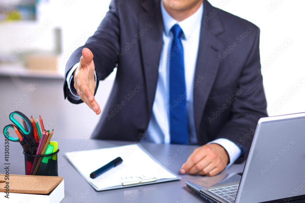 businessman sitting at desk holds out his hand for a handshake businessman sitting at desk holds out his hand for a handshake
