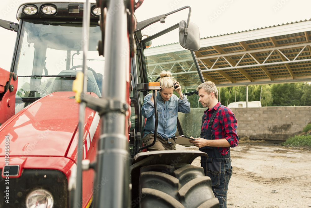 Couple discussing over document by tractor at farm Couple discussing over document by tractor at farm
