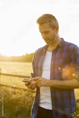 Man using phone while standing on field against sky photo